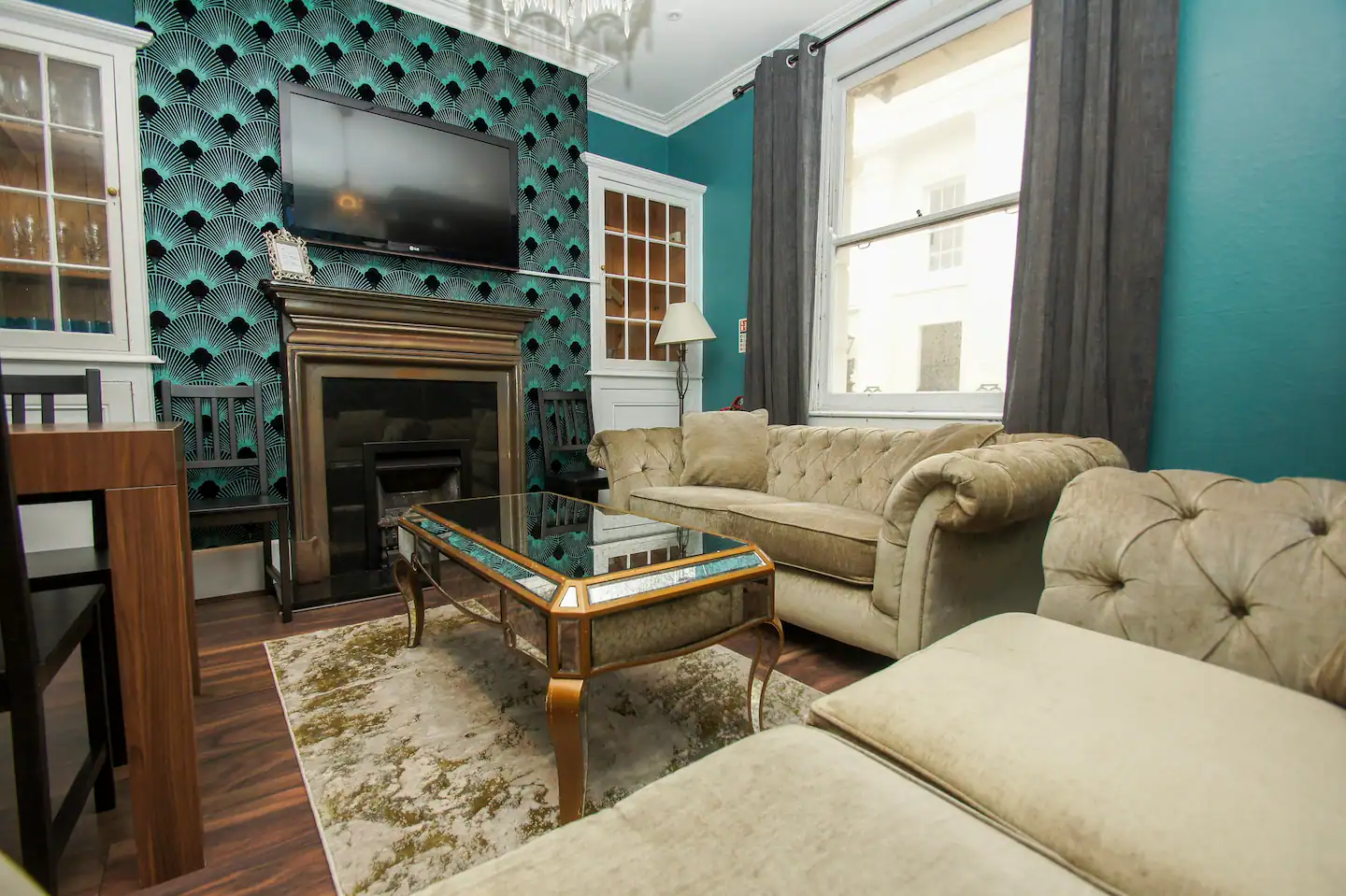 There are two velvet chesterfield couches and two art deco fan chairs, as well as a giant wall-mounted TV and a mirrored coffee table.