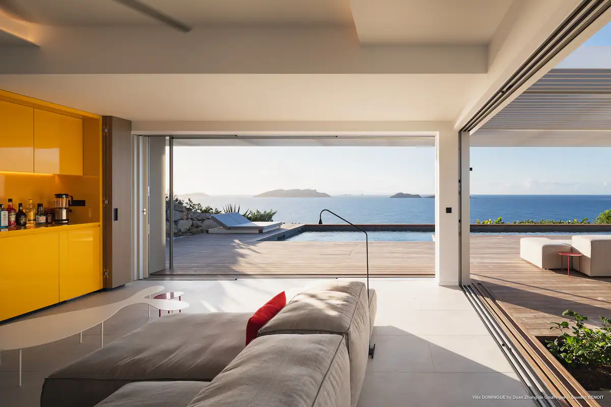 Spacious living room of the villa with floor-to-ceiling windows, offering access to a stunning pool and breathtaking views of the beach.